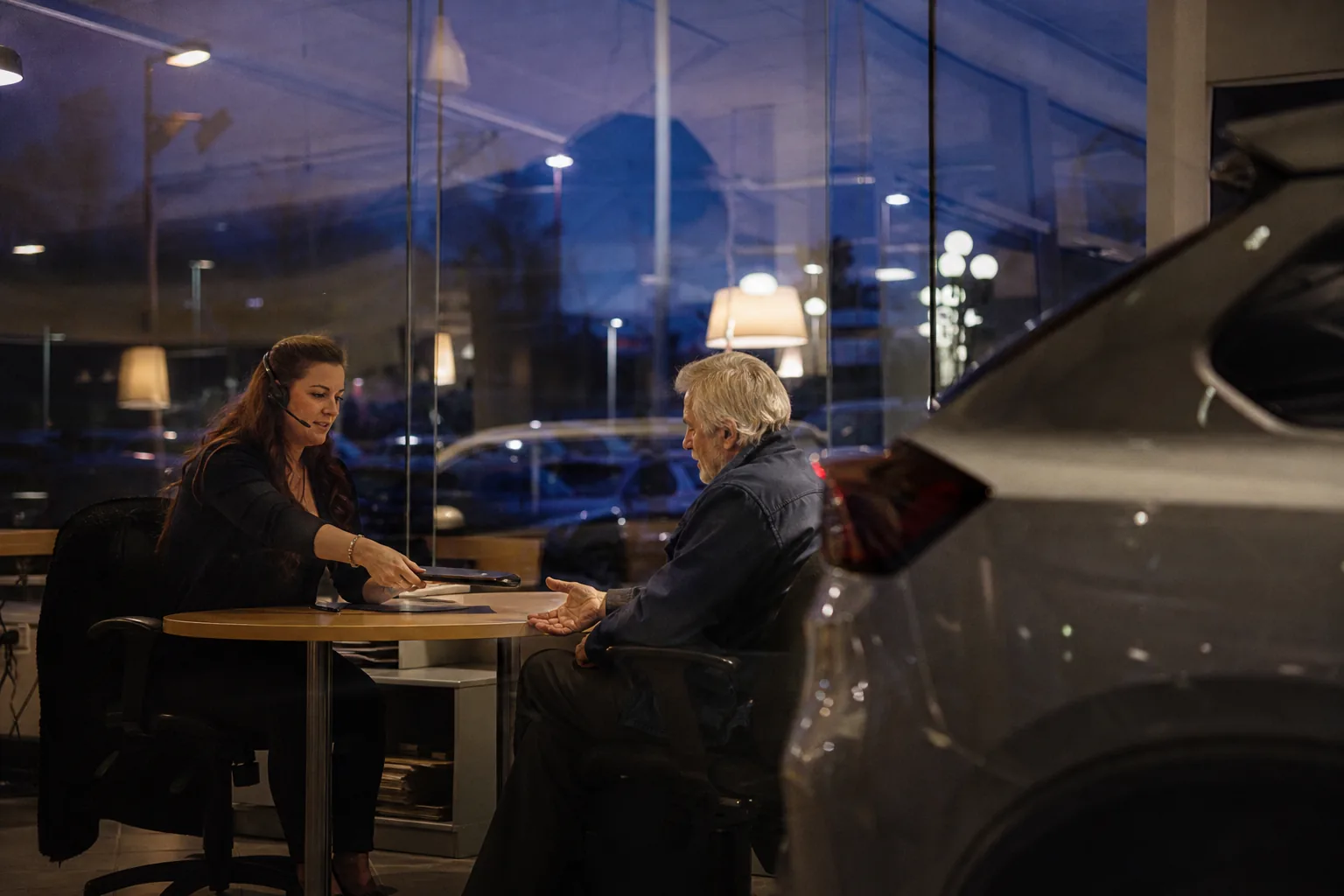 Dealership finance manager going through deal paperwork with a customer at dusk